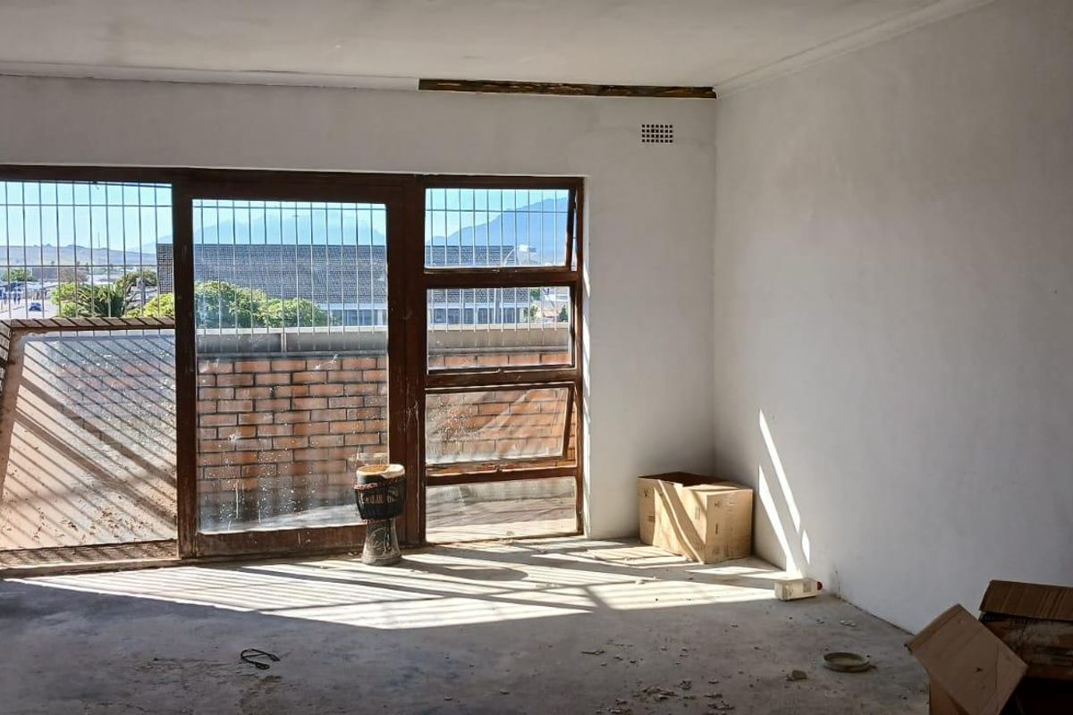 An empty, unfinished interior space featuring large glass sliding doors with security bars, offering natural light and access to an outdoor area.