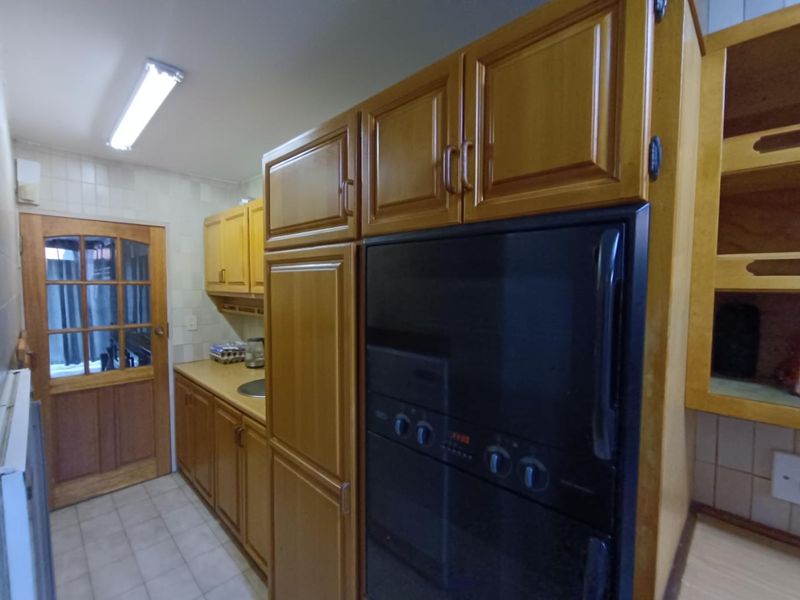 A functional kitchen featuring traditional wooden cabinetry, built-in oven, tiled backsplash, and tiled flooring with a classic timber-framed door.