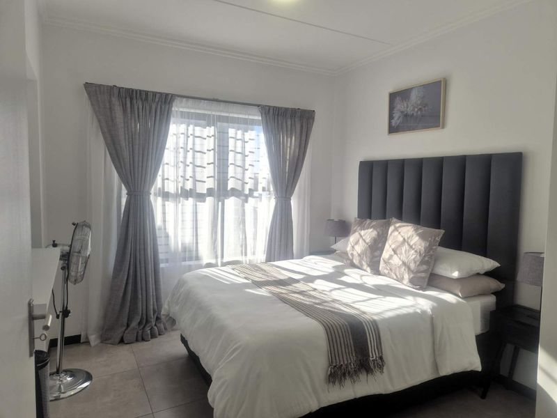 A well-lit bedroom featuring neutral tiled flooring and large windows with installed curtain tracks, providing a bright and comfortable living space.