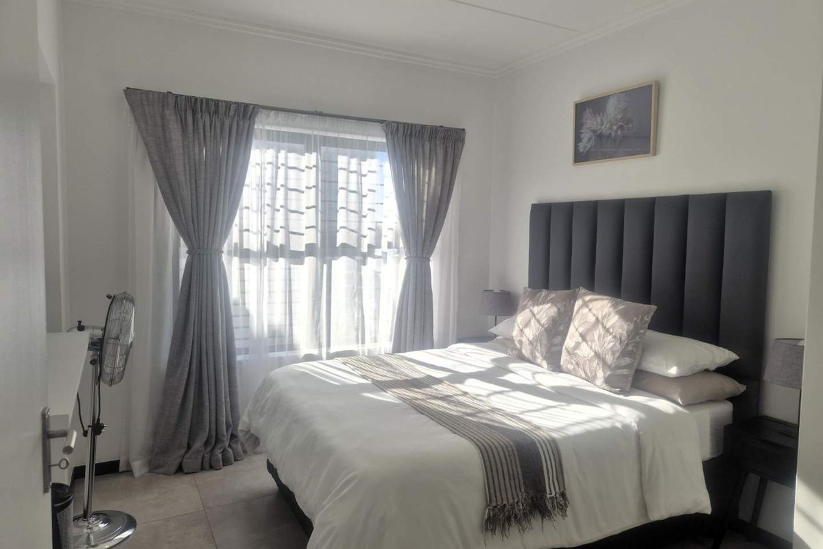 A well-lit bedroom featuring neutral tiled flooring and large windows with installed curtain tracks, providing a bright and comfortable living space.