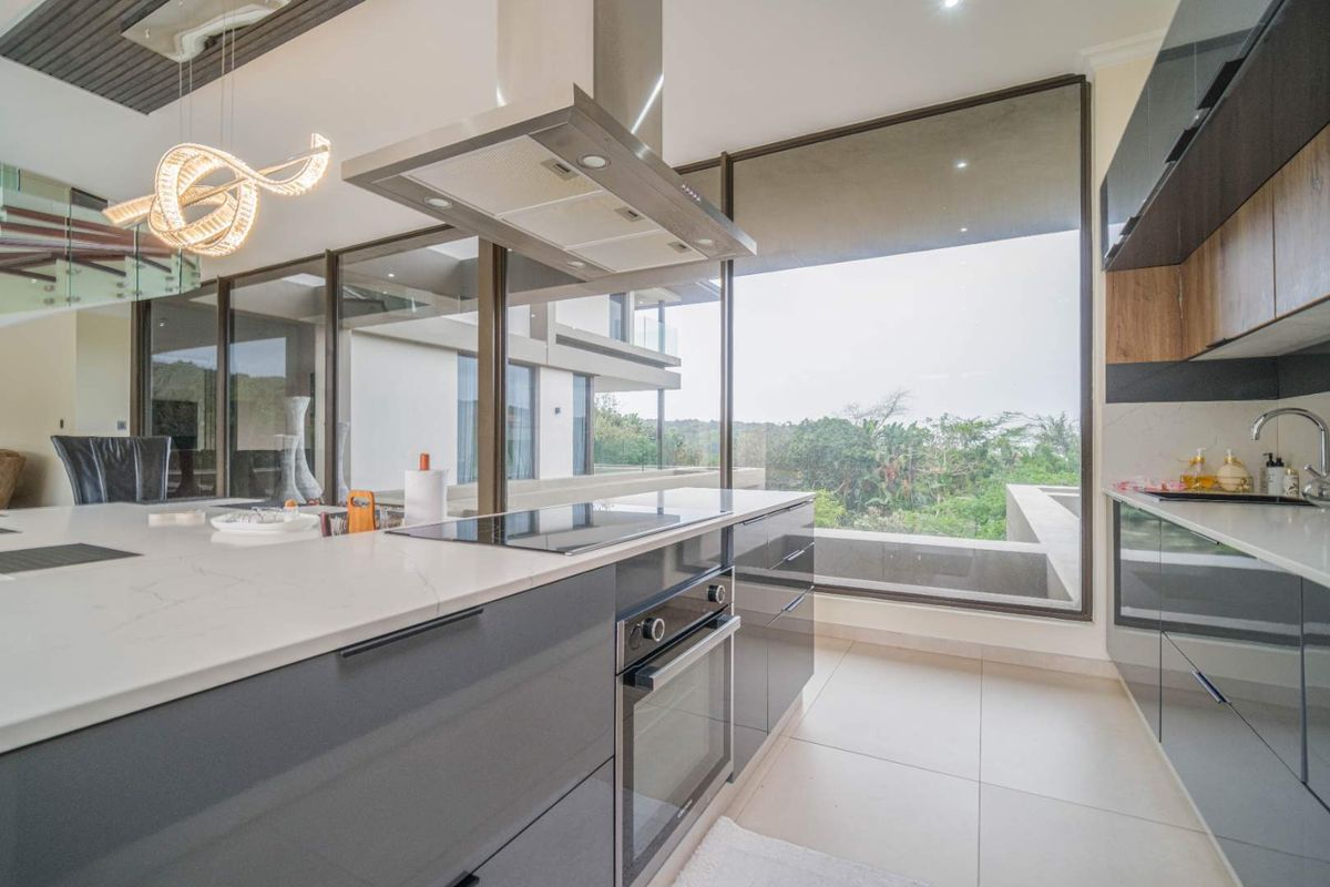 Modern kitchen featuring sleek cabinetry, stone countertops, integrated oven, induction hob, and a stainless steel extractor fan with expansive floor-to-ceiling windows.