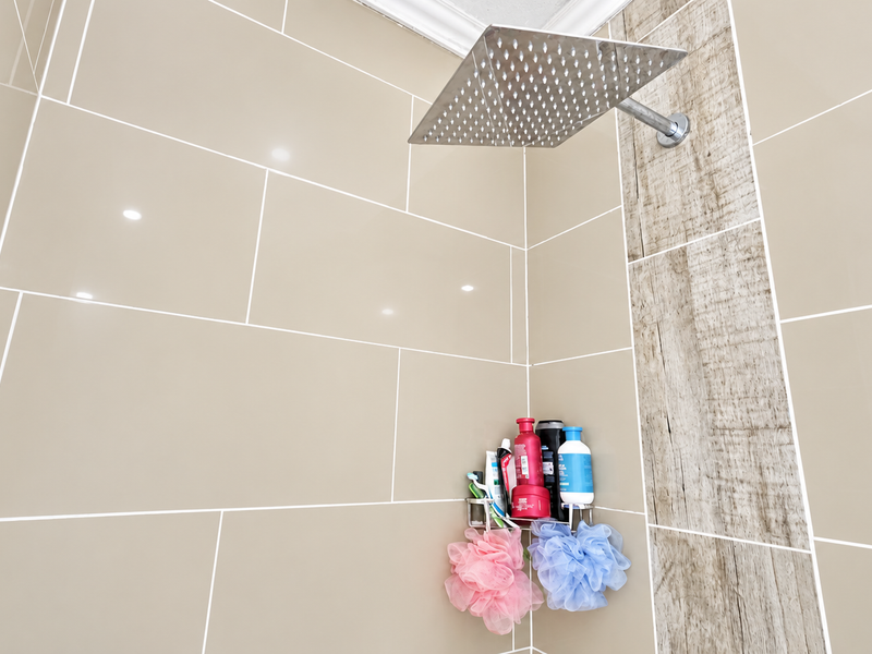 A modern shower enclosure featuring large format beige wall tiles, a wood-look accent strip, and a contemporary square rainfall shower head.