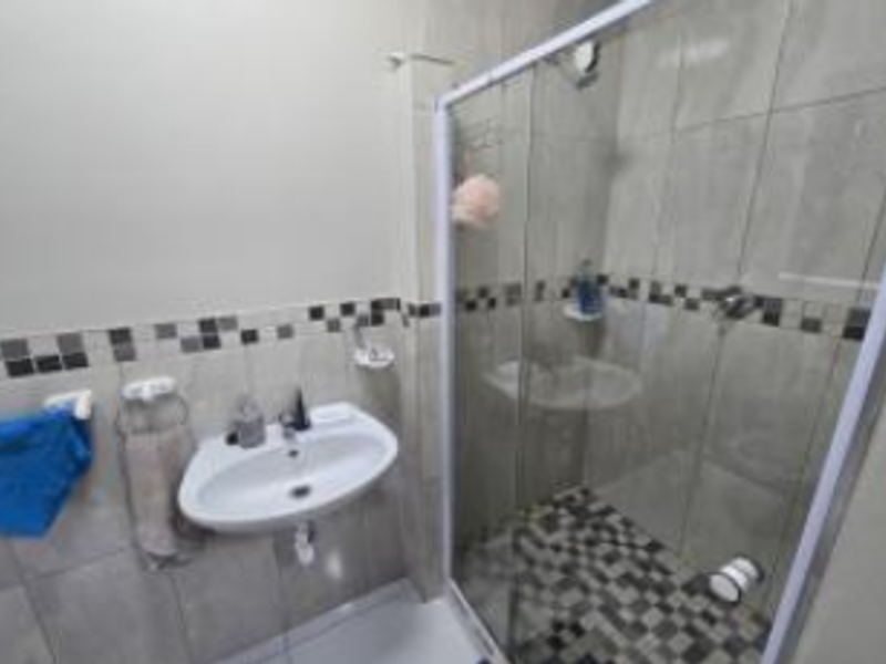 A functional bathroom featuring a wall-mounted basin, a glass-enclosed shower with mosaic tile accents, and neutral wall tiling.