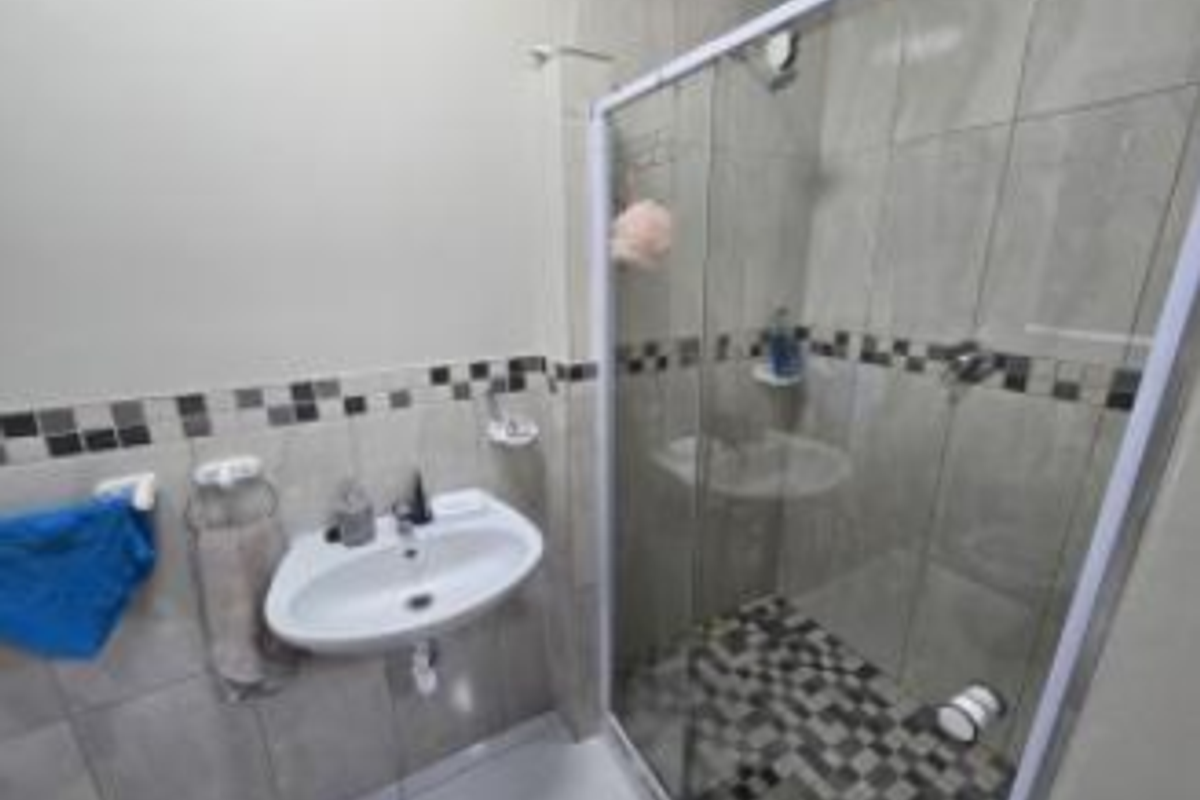 A functional bathroom featuring a wall-mounted basin, a glass-enclosed shower with mosaic tile accents, and neutral wall tiling.