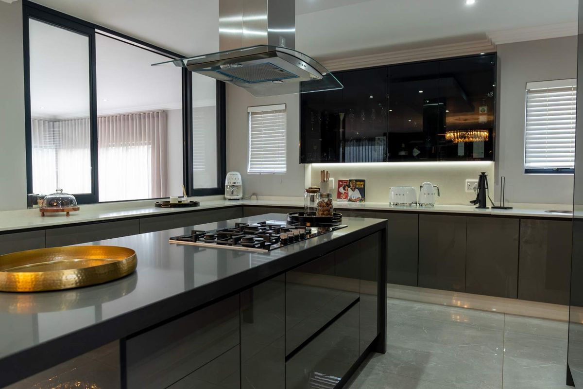 Modern kitchen featuring a central island with a built-in gas hob, sleek high-gloss cabinetry, stone countertops, and a stainless steel extractor fan.