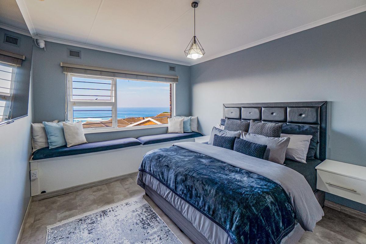 A well-maintained bedroom featuring a built-in window seat with ocean views, modern pendant lighting, and neutral wall finishes.