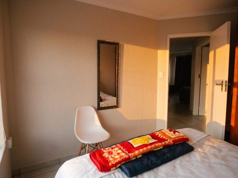 A bedroom featuring textured wall finishes and tiled flooring, illuminated by warm natural light, with an open doorway leading to an adjacent living space.
