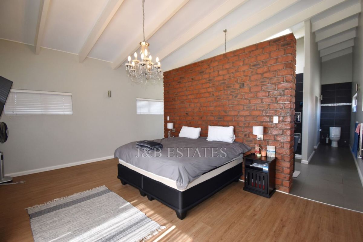 Spacious bedroom featuring a striking exposed brick feature wall, vaulted ceilings with exposed beams, and an en-suite bathroom area.