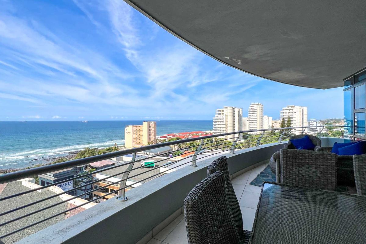 Spacious covered balcony featuring tiled flooring, stainless steel and glass balustrades, offering expansive panoramic ocean and coastal views.
