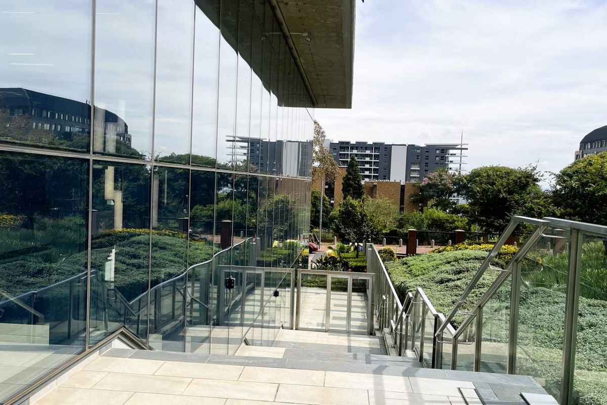 Modern outdoor staircase with glass balustrades and tiled steps, leading to a landscaped garden area with contemporary architectural glass facade.