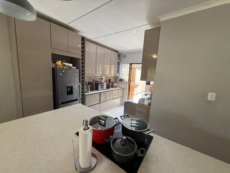 Modern kitchen featuring high-gloss cabinetry, stone countertops, and a central island with an integrated electric hob, leading to an outdoor area.