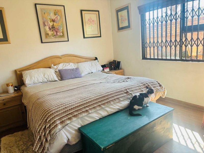 A functional bedroom featuring laminate flooring and a window fitted with a security gate for added protection.