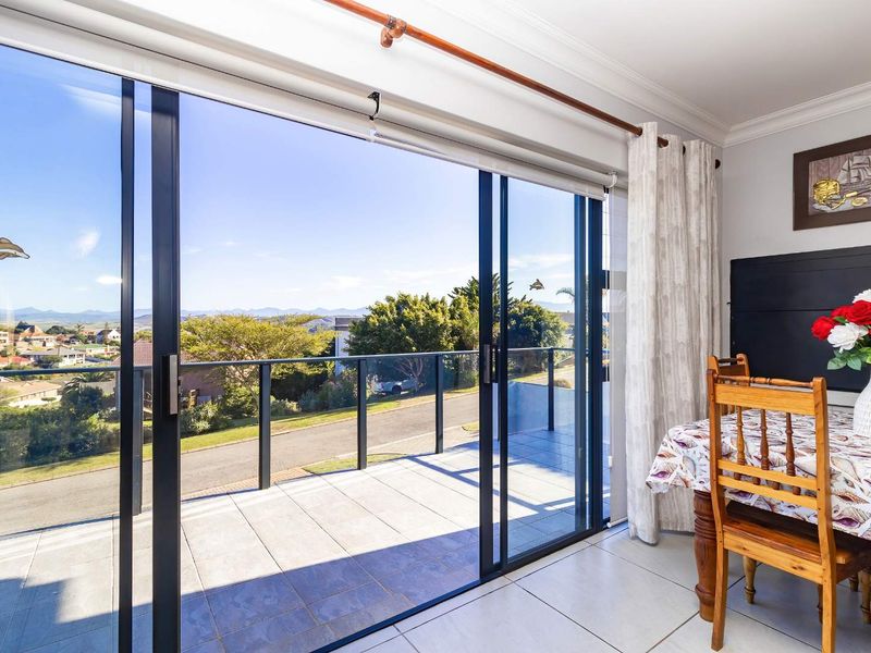 A bright indoor dining area featuring large sliding glass doors that open onto a tiled balcony with scenic neighborhood views.