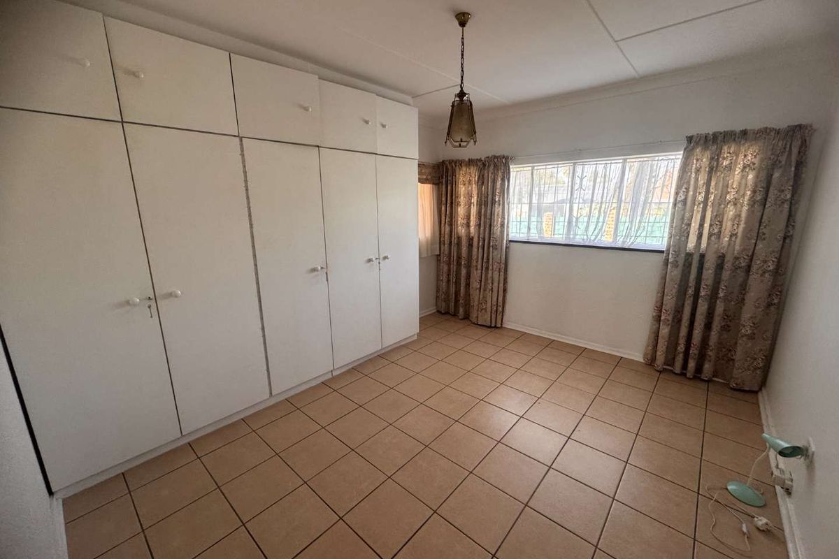 A vacant bedroom featuring neutral tiled flooring and extensive built-in cupboard storage, offering a clean canvas for personalization.