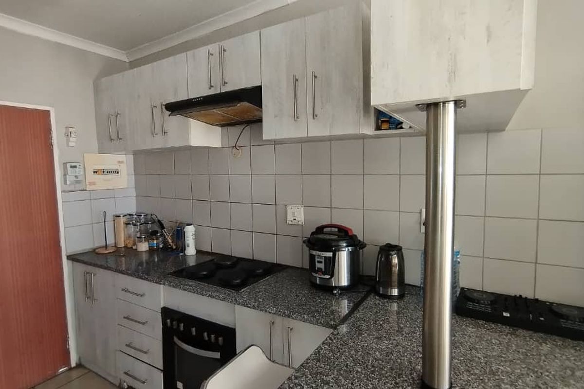 A functional kitchen featuring granite countertops, built-in oven, electric hob, extractor fan, and ample cabinetry with a breakfast bar.