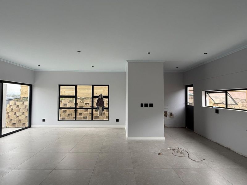 Spacious open-plan living area featuring large black aluminium windows, sliding doors, tiled flooring, and recessed lighting, currently in an unfinished state.