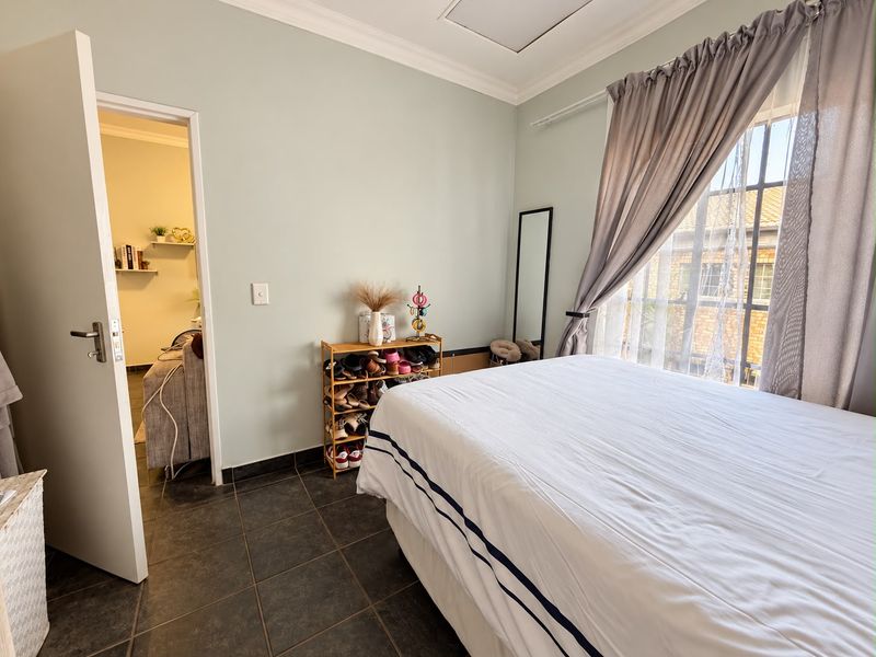 A bedroom featuring tiled flooring, a window with security bars, and neutral wall tones, offering a functional and well-maintained living space.