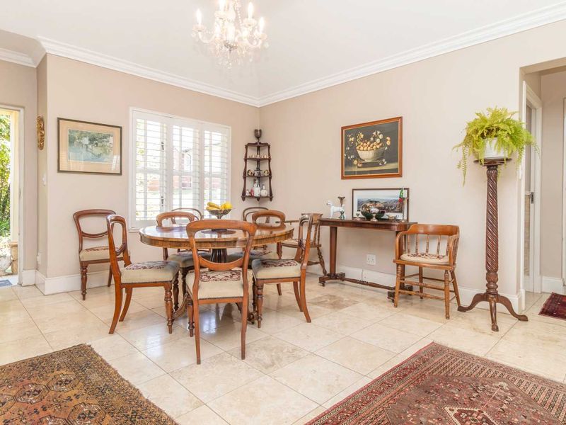 A bright and elegant dining room featuring polished stone tile flooring, crown molding, a classic crystal chandelier, and plantation shutters.