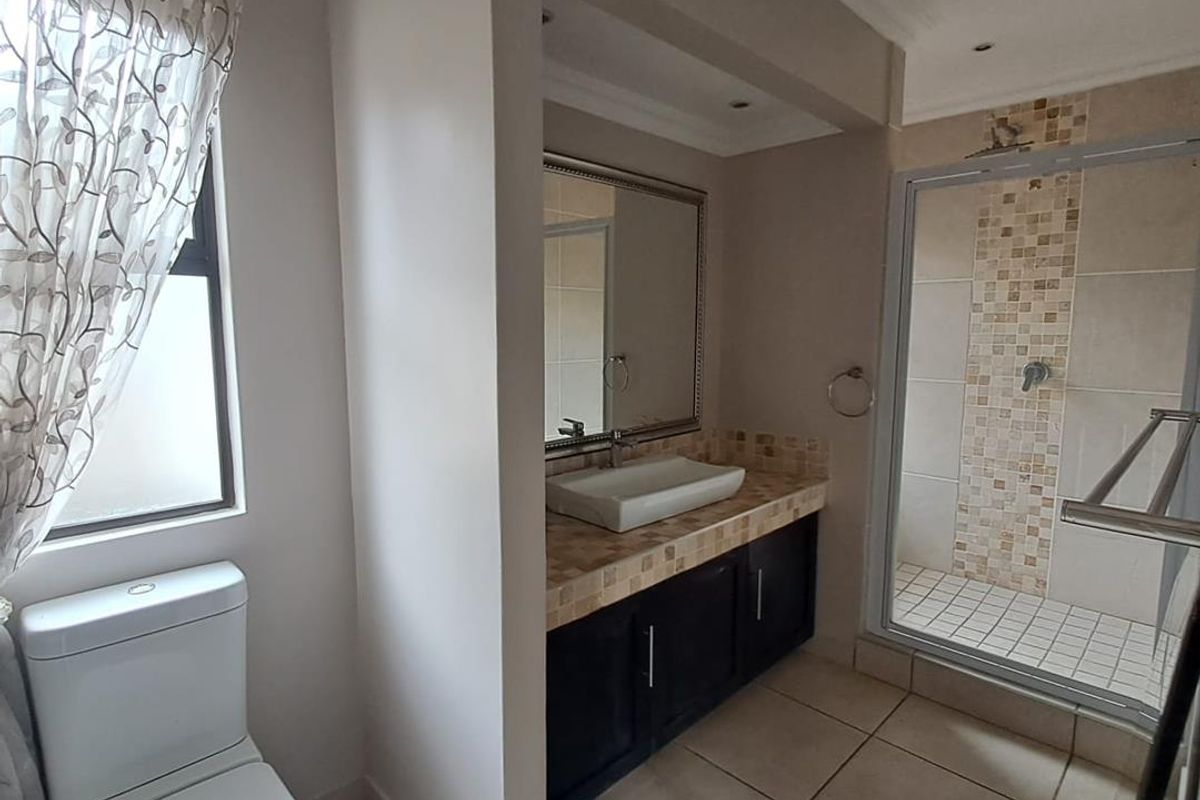 A well-maintained bathroom featuring a modern vessel sink on a vanity cabinet, a tiled shower enclosure, and neutral floor tiling.