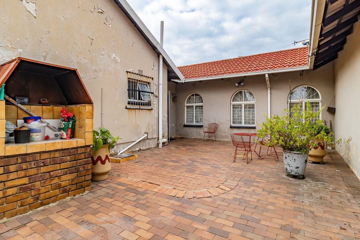 A paved rear courtyard featuring a built-in brick braai area, arched windows, and significant exterior wall maintenance required.