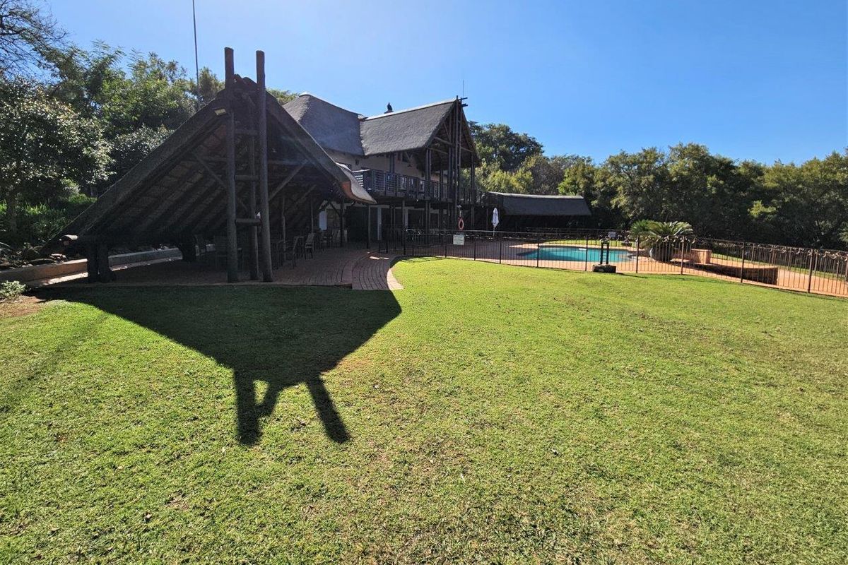 Spacious rear garden featuring a well-maintained lawn, a swimming pool with safety fencing, and a large thatched-roof outdoor entertainment area.