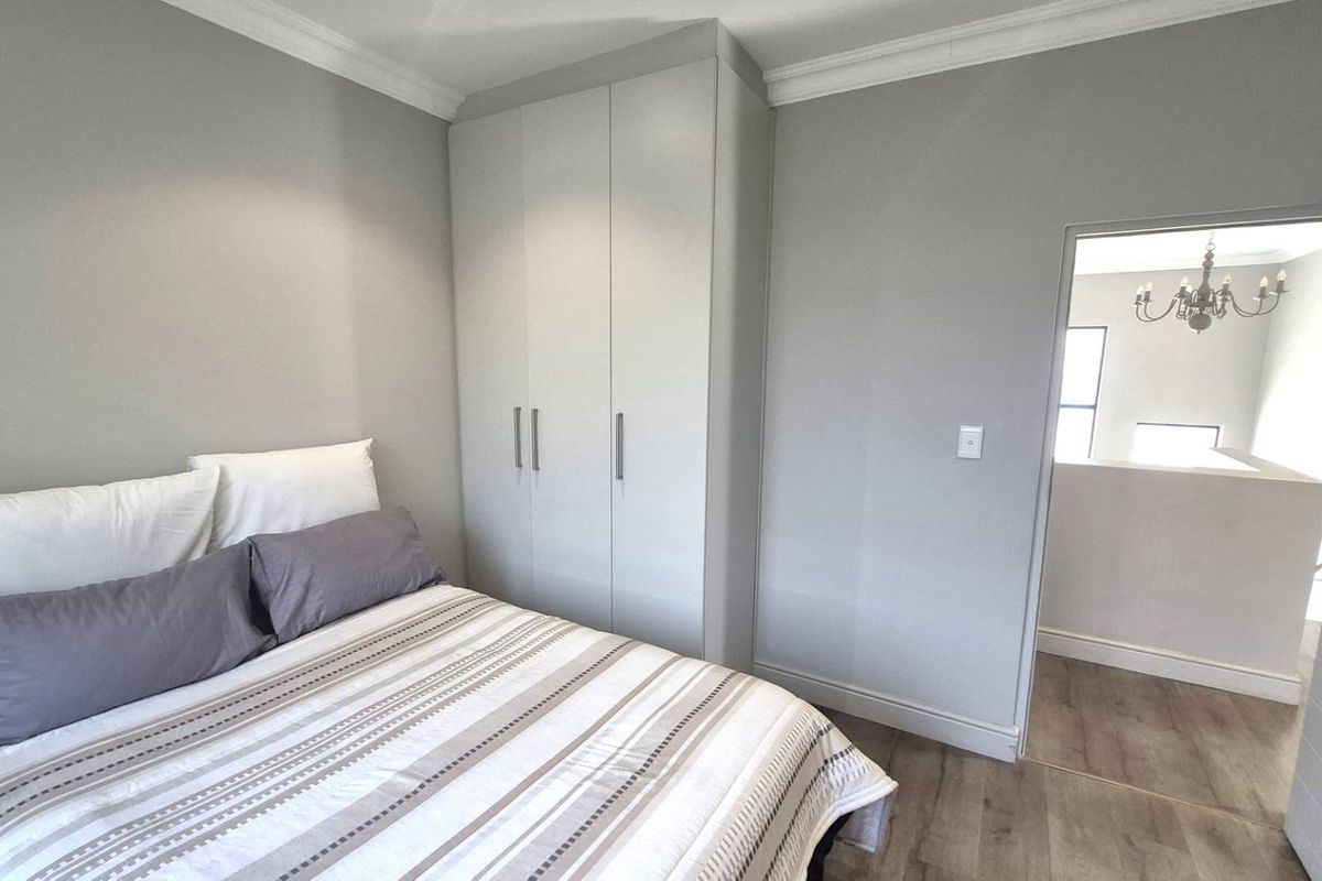 A well-maintained bedroom featuring neutral grey walls, built-in cupboards, and modern laminate flooring, offering a clean and contemporary living space.