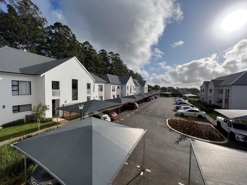 Aerial view of an apartment complex featuring paved parking areas with shade cloth carports and well-maintained landscaped garden beds.