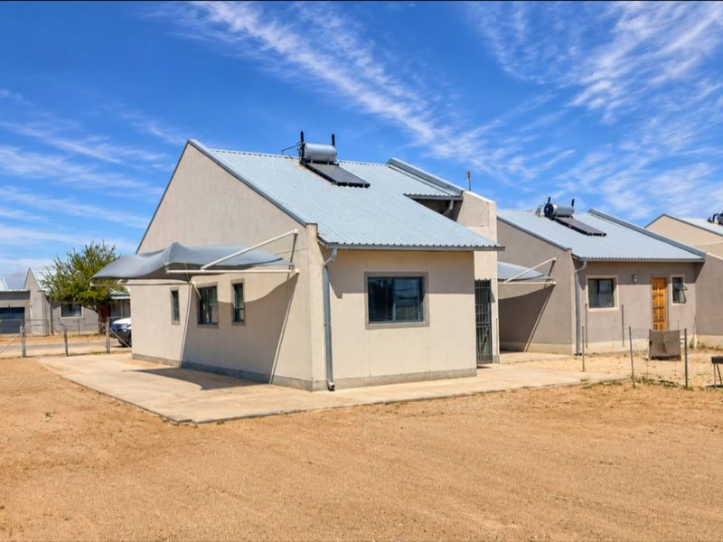 Rear view of a modern house featuring a corrugated metal roof with solar water heating, a concrete patio, and installed shade sails.