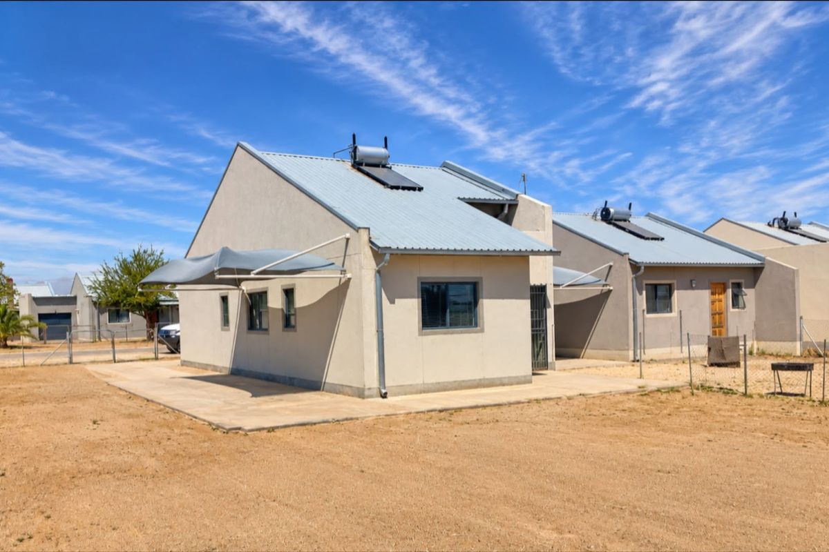 Rear view of a modern house featuring a corrugated metal roof with solar water heating, a concrete patio, and installed shade sails.