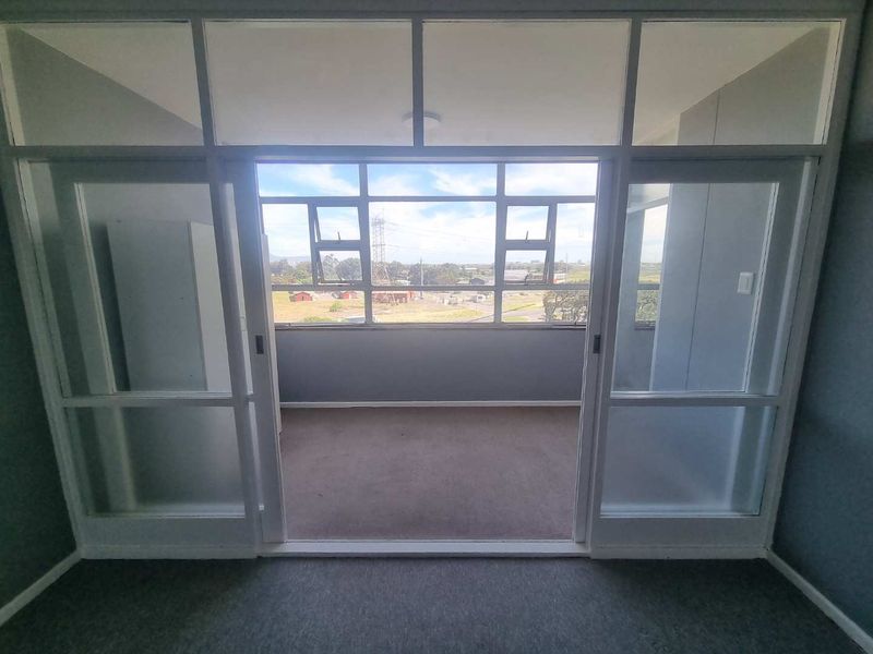 An enclosed balcony or sunroom featuring large glass panels and sliding doors, offering an open view and potential for a bright seating area.
