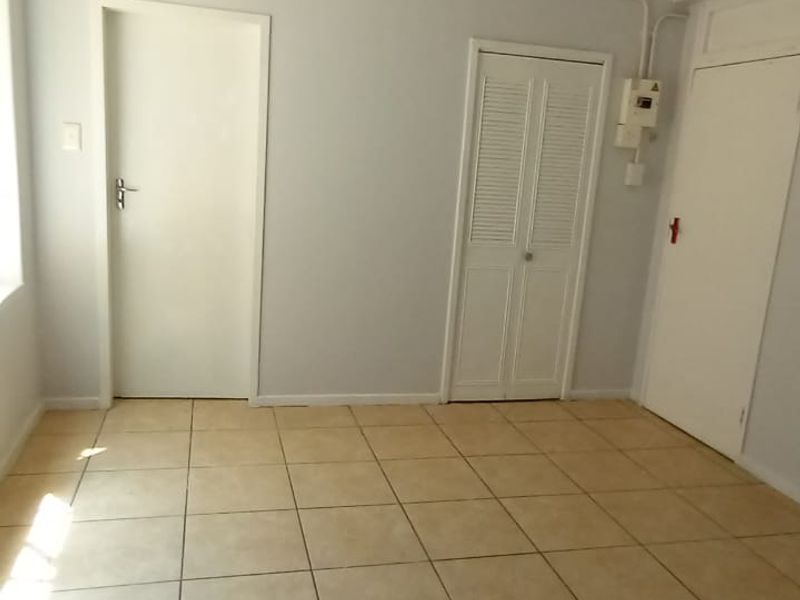 An empty living area featuring neutral tiled flooring, multiple interior doors, and a built-in closet with louvered doors.