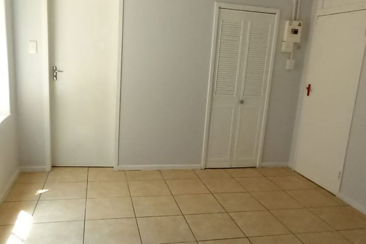 An empty living area featuring neutral tiled flooring, multiple interior doors, and a built-in closet with louvered doors.