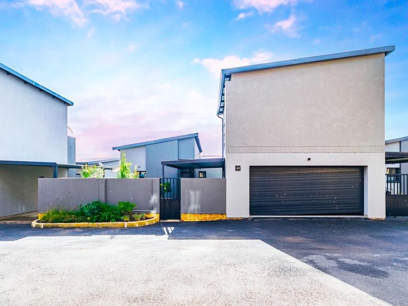 Front elevation of a modern townhouse featuring a roller garage door, paved driveway, and secure pedestrian access gate.