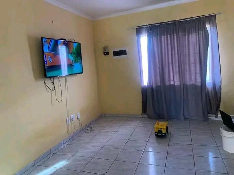 A simple living room area featuring tiled flooring and wall-mounted electrical points, offering a blank canvas for potential interior updates.