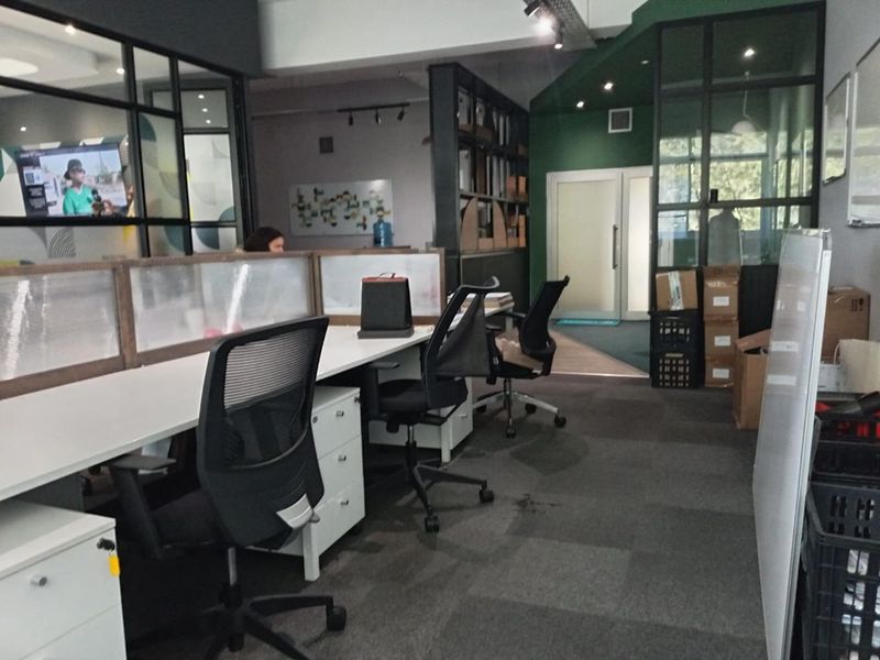 Modern open-plan office space featuring glass partition walls, recessed track lighting, and professional carpeted flooring with integrated shelving units.