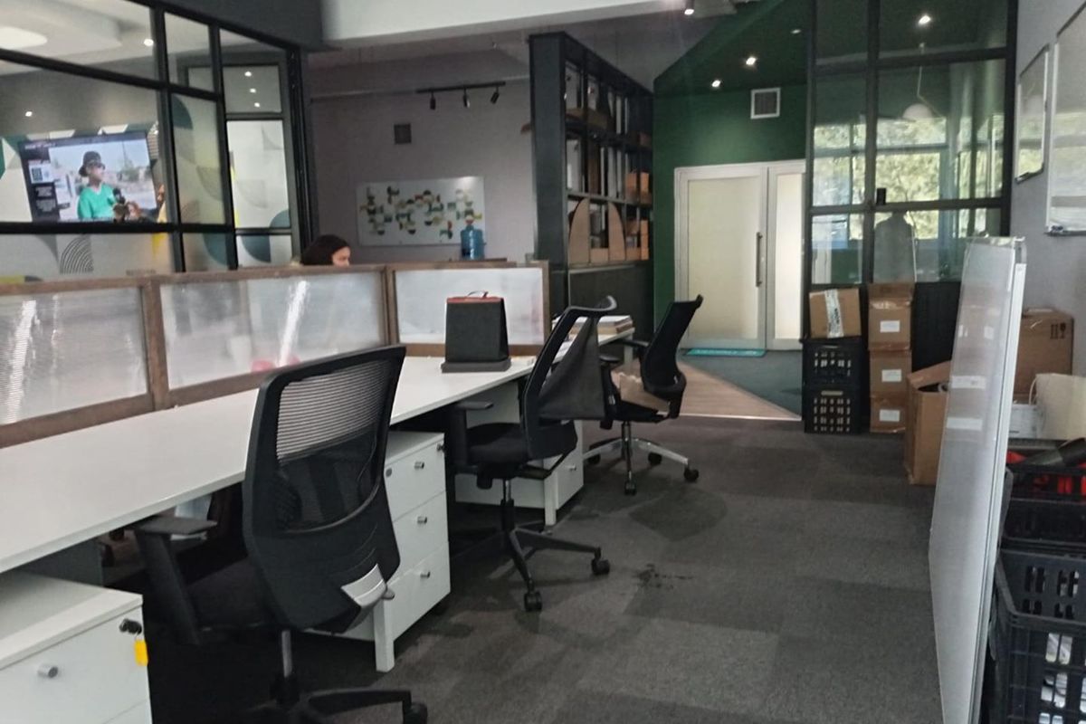 Modern open-plan office space featuring glass partition walls, recessed track lighting, and professional carpeted flooring with integrated shelving units.