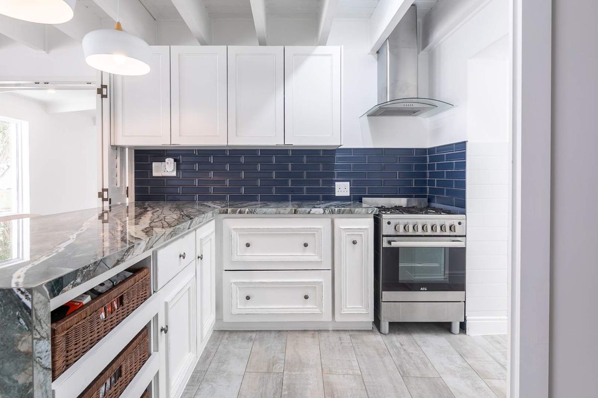 Modern kitchen featuring white shaker cabinetry, striking dark stone countertops, blue subway tile backsplash, and a stainless steel gas stove with extractor fan.