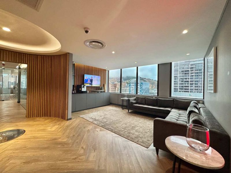 Modern office lounge area featuring elegant herringbone timber flooring, sophisticated slatted wood wall paneling, and expansive windows offering panoramic city views.
