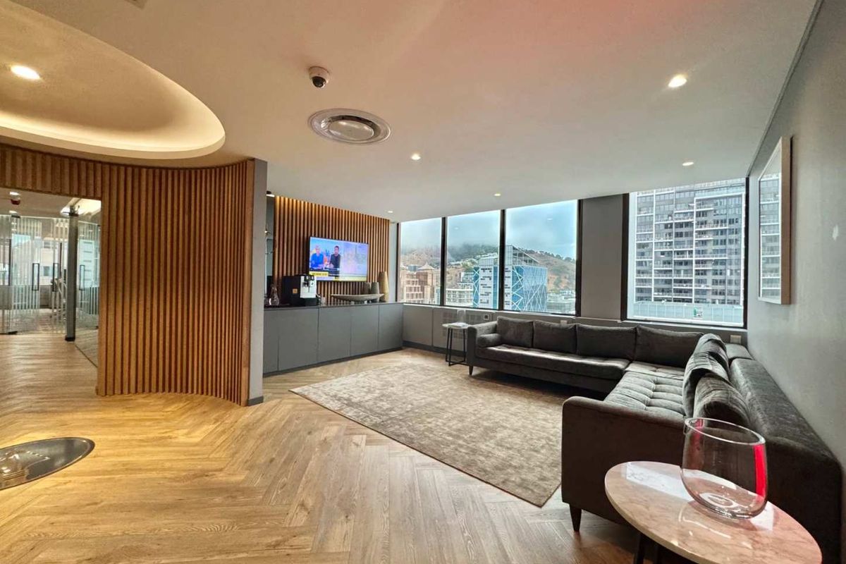 Modern office lounge area featuring elegant herringbone timber flooring, sophisticated slatted wood wall paneling, and expansive windows offering panoramic city views.