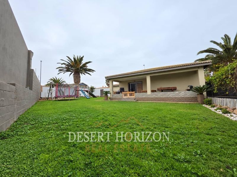 Spacious rear garden featuring a well-maintained lawn, a covered patio area with brick detailing, and secure boundary walls.