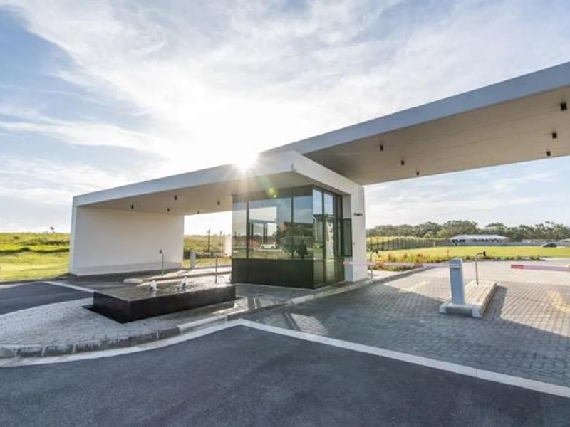 Modern security gatehouse entrance featuring a sleek canopy, boom gate access control, and a decorative water feature at the estate entry.