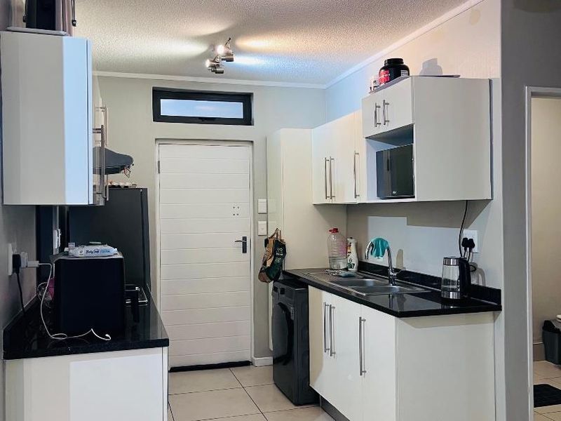A functional kitchen featuring white cabinetry, black granite countertops, tiled flooring, and integrated lighting, providing a clean and practical workspace.
