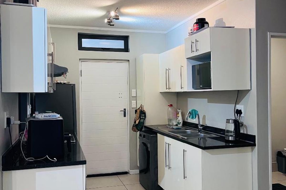 A functional kitchen featuring white cabinetry, black granite countertops, tiled flooring, and integrated lighting, providing a clean and practical workspace.