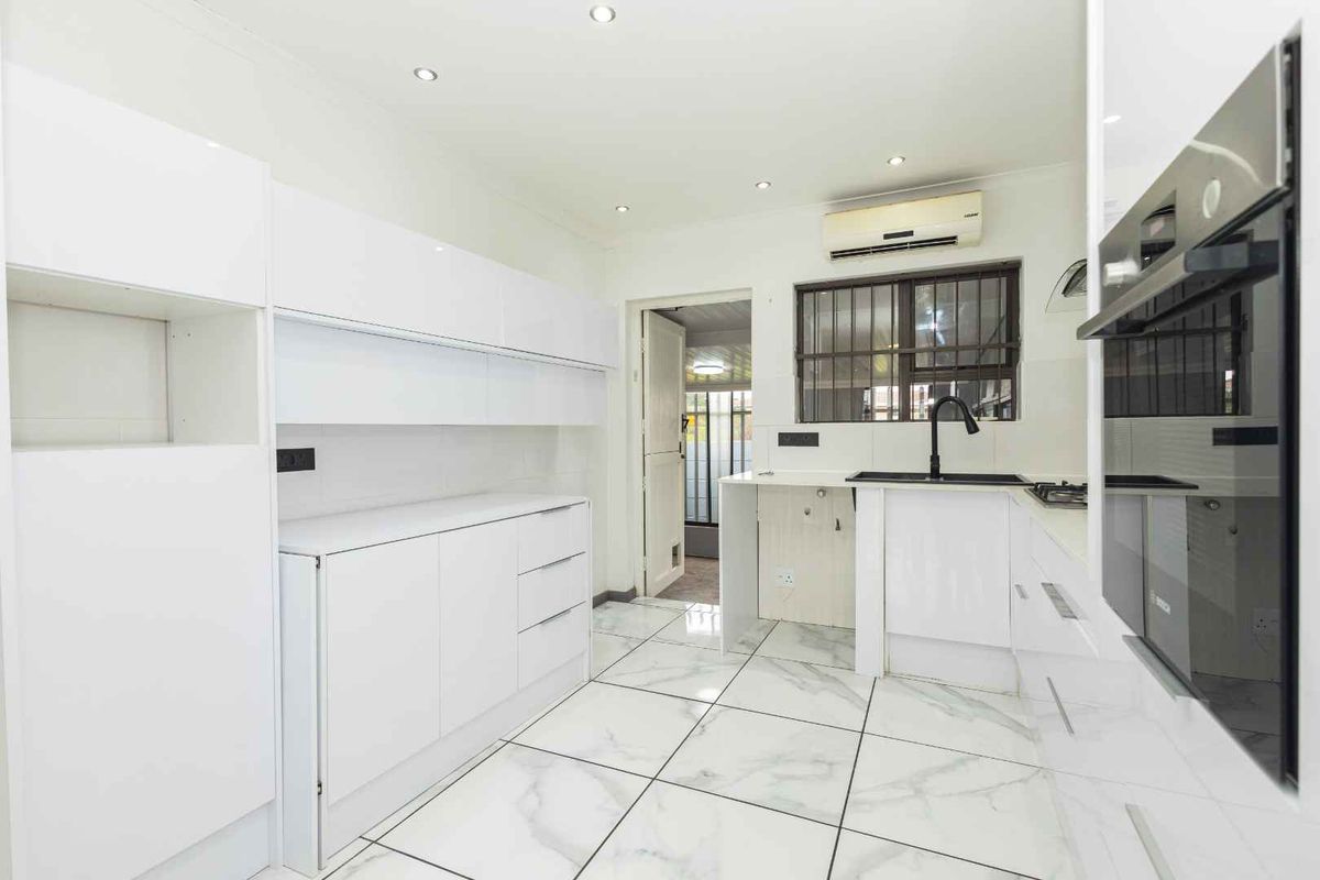 Modern white kitchen featuring marble-look floor tiles, built-in oven, gas hob, and black fixtures. The space is clean and ready for final finishing touches.