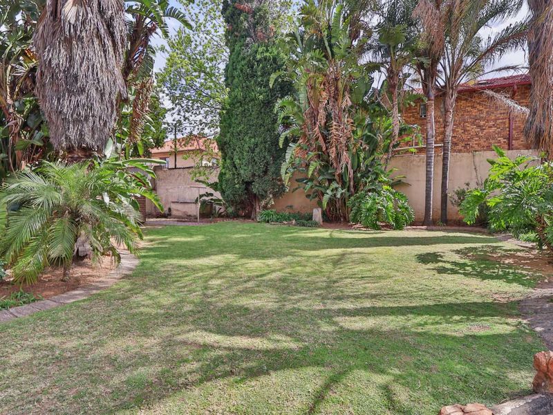 A spacious, well-established garden featuring a lush lawn, mature trees, and a secure perimeter wall with stone edging.