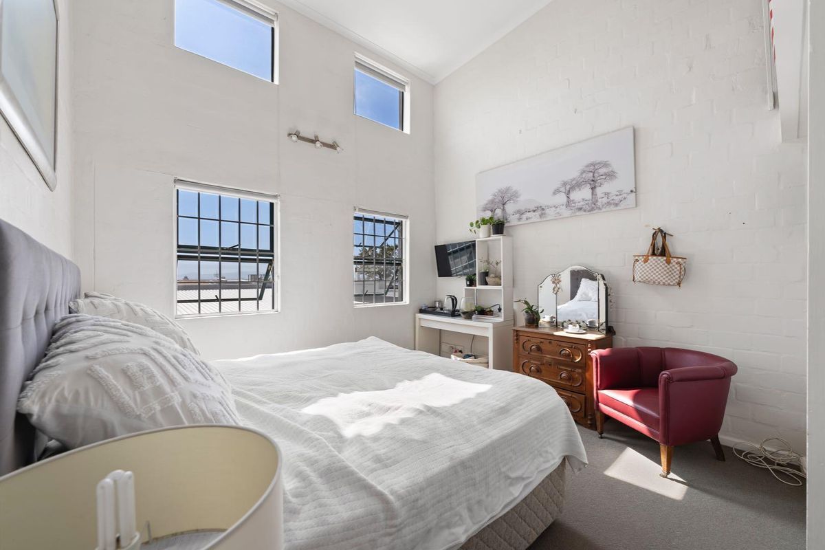 A bright bedroom featuring double-height ceilings, exposed brick walls, and clerestory windows that provide ample natural light.