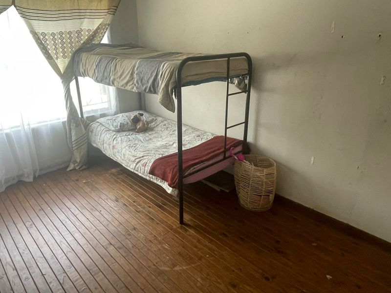 A bedroom featuring timber flooring and a window, currently requiring cosmetic attention to the wall surfaces.