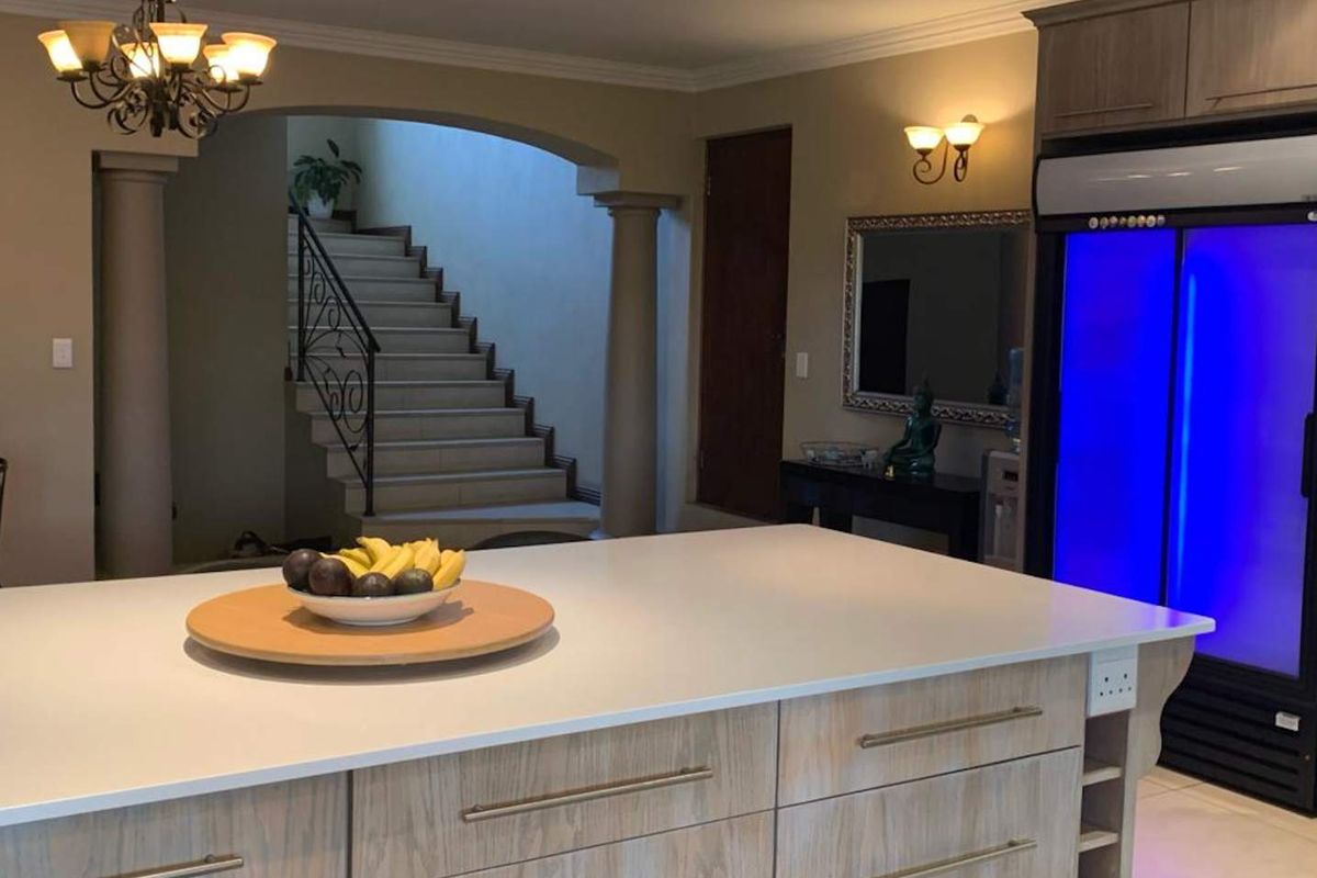 A spacious kitchen featuring a large central island with stone countertops, light wood cabinetry, and an open-plan layout leading to a staircase.