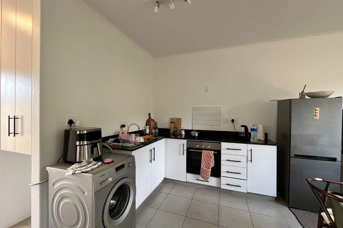 A functional kitchen featuring white cabinetry, dark countertops, a subway tile backsplash, and integrated oven and hob, with tiled flooring throughout.