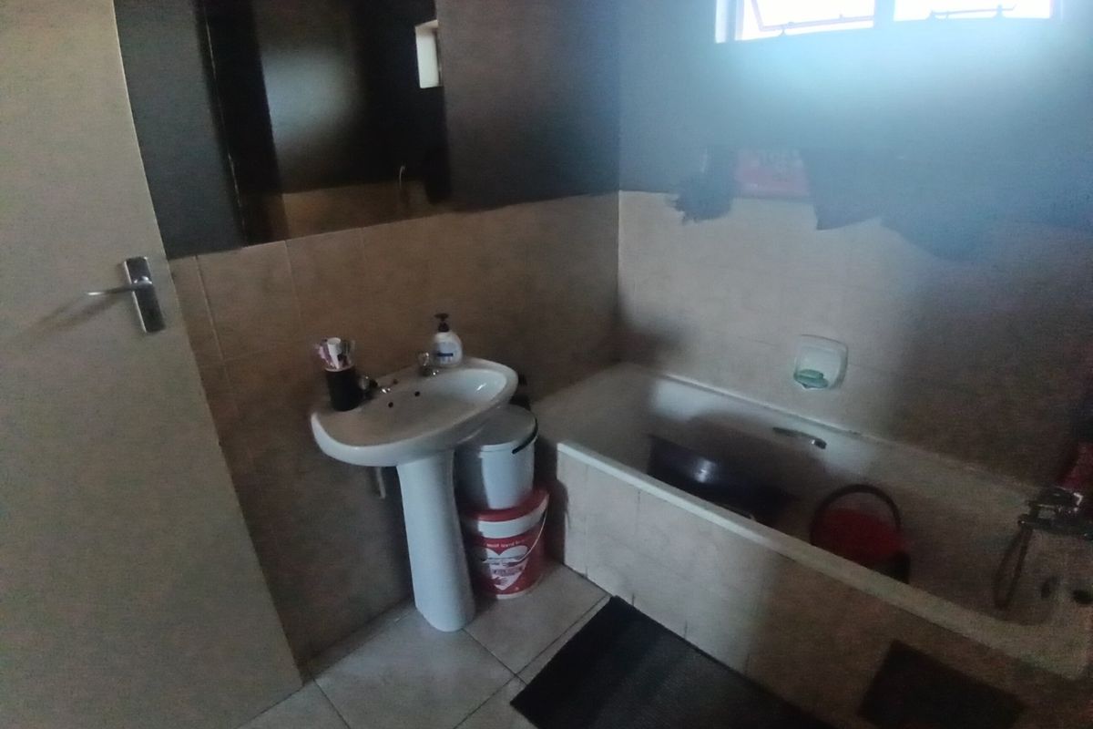 A functional bathroom featuring a pedestal basin, bathtub, and tiled finishes, offering a standard layout suitable for modernization.